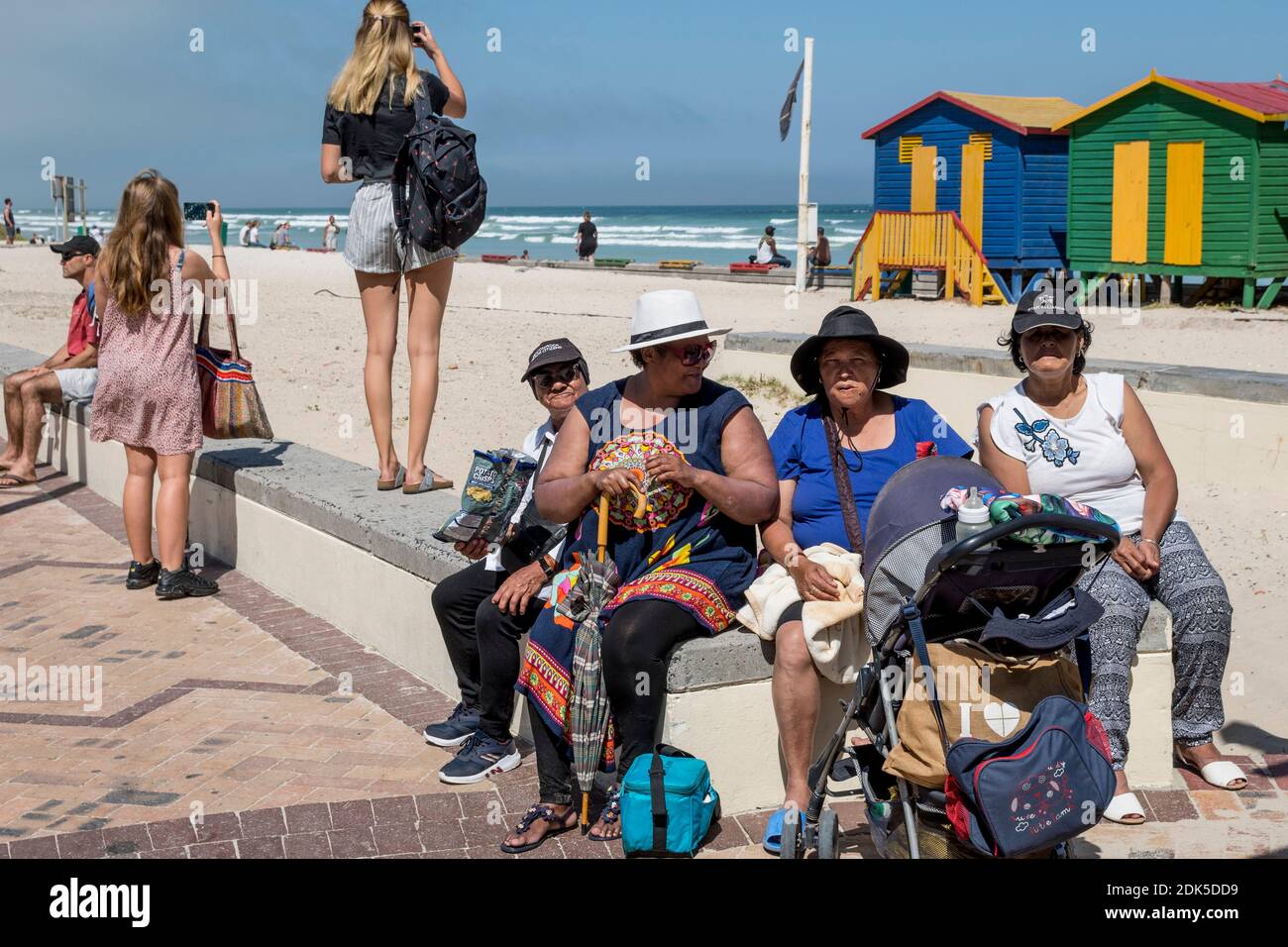 Un groupe social communautaire de femmes sur une sortie à Surferss' Corner, plage de Muizenberg, le Cap, Afrique du Sud. Cabines de plage peintes en bois en arrière-plan. Banque D'Images