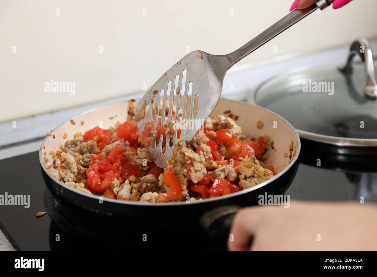 la jeune femme au foyer fait frire de la viande dans une poêle et une cuisinière électrique. Dîner de cuisine à la maison. Banque D'Images