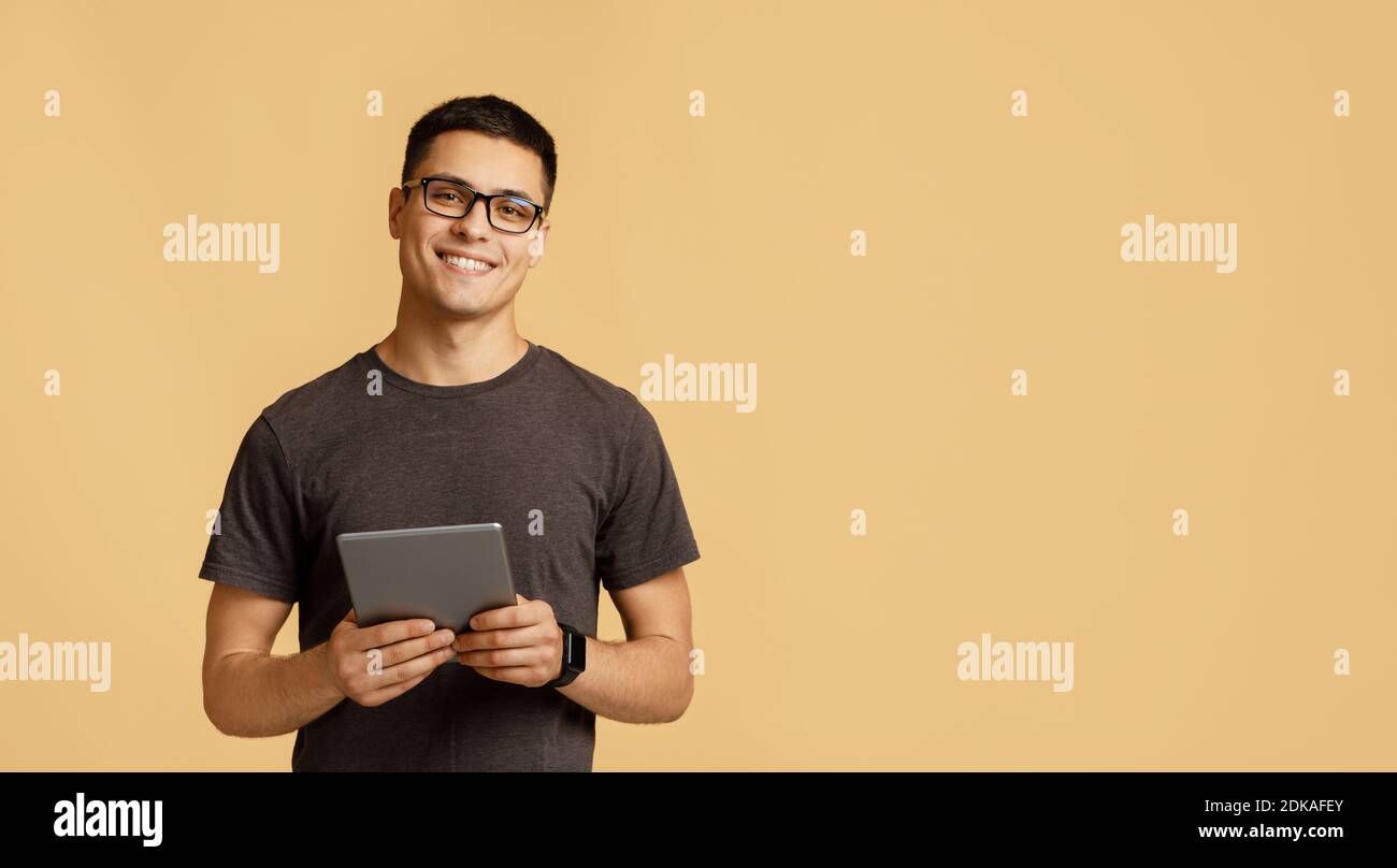 Gai jeune homme attrayant en lunettes regarde l'appareil photo, tient la tablette numérique sur la leçon en ligne Banque D'Images