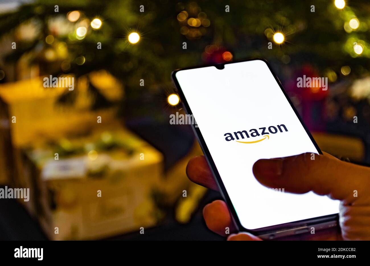 Application Amazon, application shopping en ligne, icône affichée sur le smartphone avec le doigt, sapin de Noël et cadeaux en arrière-plan Banque D'Images