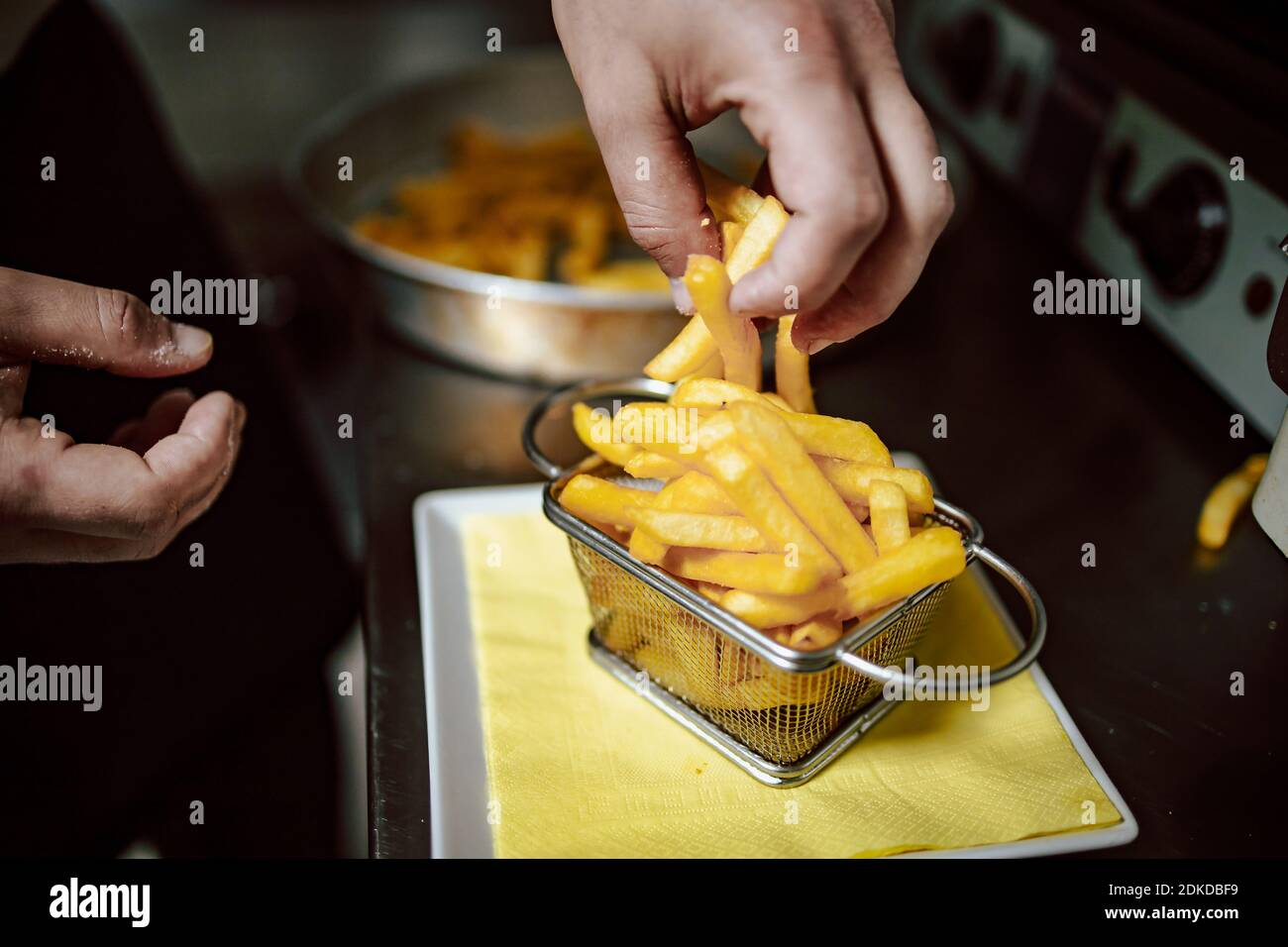 Gros plan des mains du chef qui organisent les frites dans un petit panier métallique au restaurant. Prêt à servir Banque D'Images