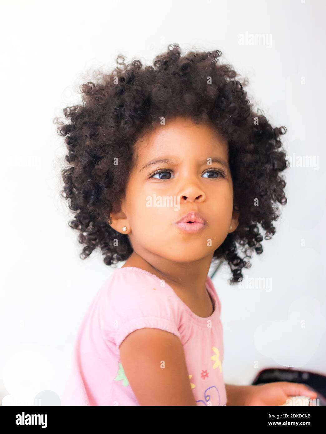 Gros Plan De Baby Girl Avec Des Cheveux Noirs De Boucle Contre Le Mur Blanc Photo Stock Alamy
