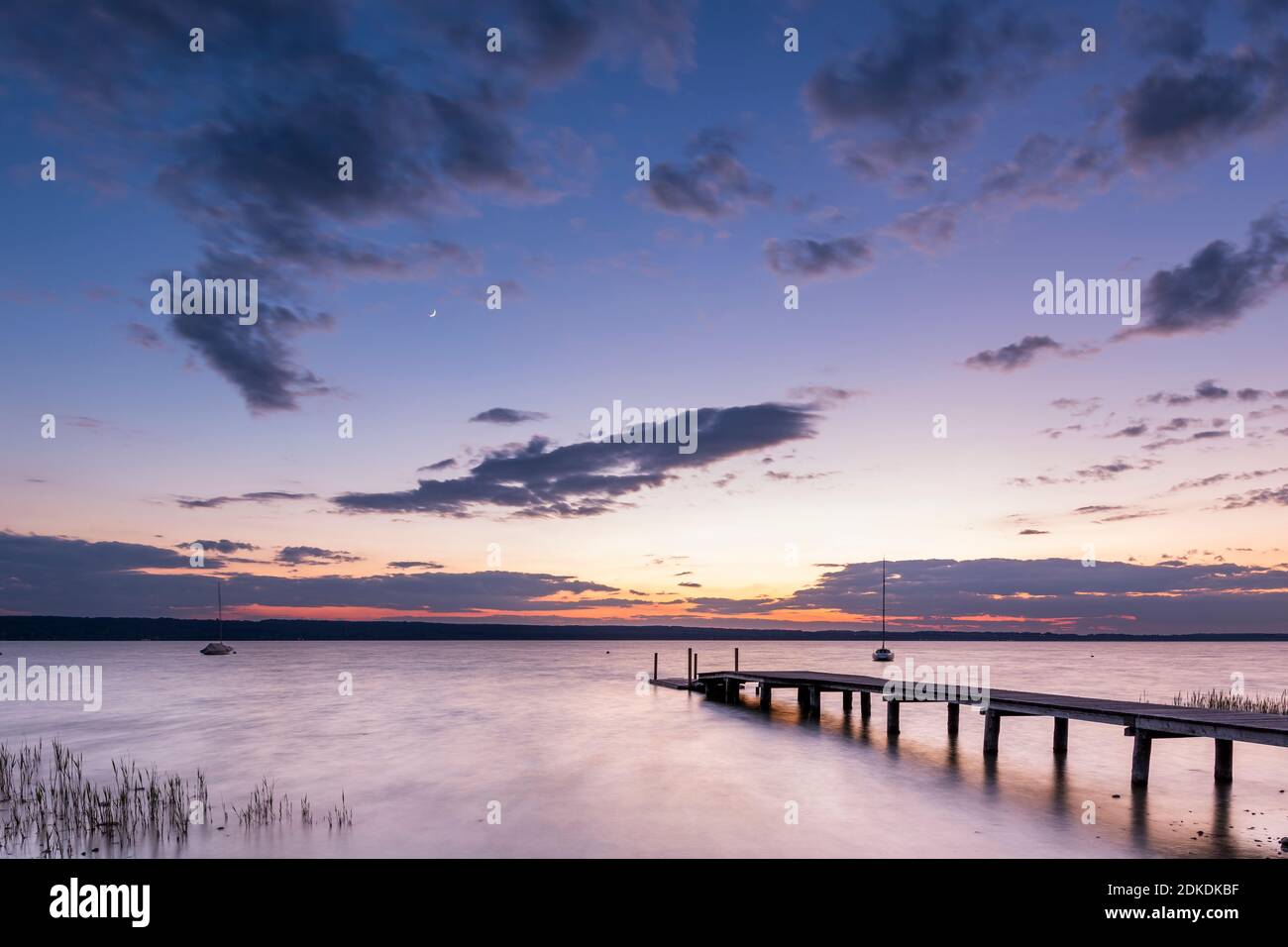 Ambiance nocturne sur l'une des innombrables allées en bois de l'Ammersee près de Wartaweil, en arrière-plan la lune, les couleurs et les bateaux à voile individuels ancrés. Banque D'Images