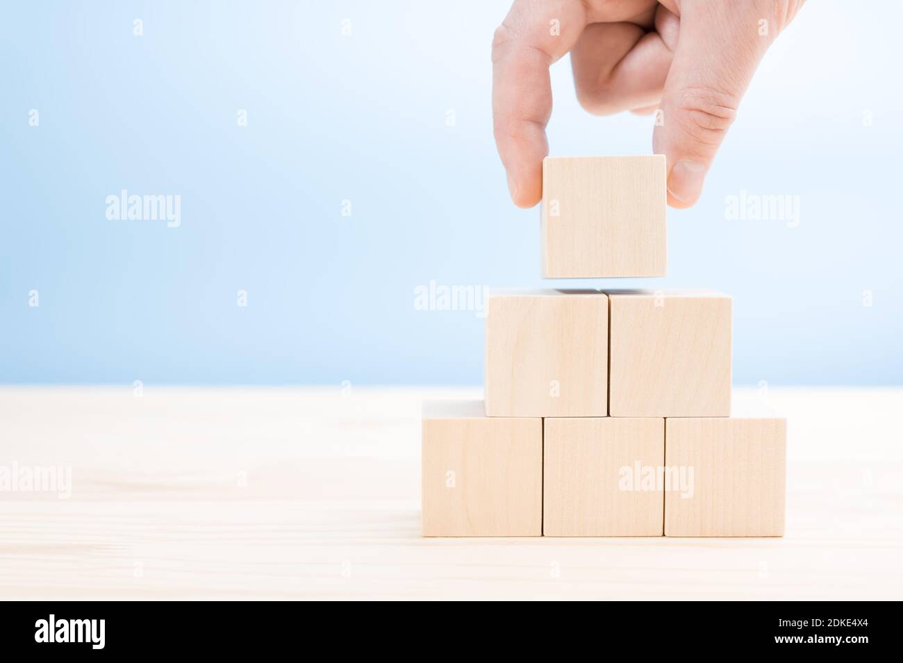 la main pose construit une pyramide de cubes de bois vierges. Un bloc de bois en forme de cube empilé en forme de pyramide sans graphiques pour le concept de conception d'entreprise. Banque D'Images