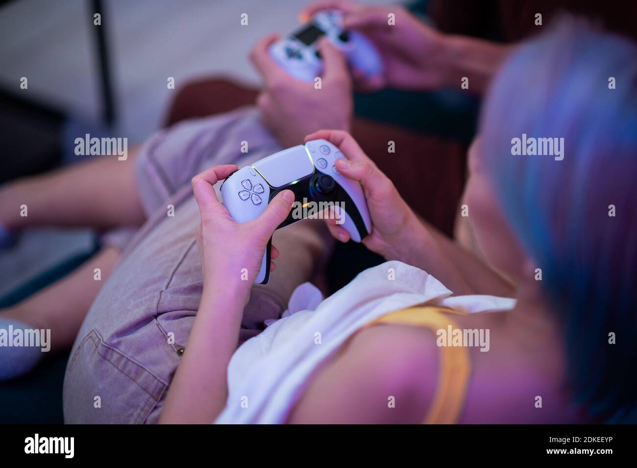 Couple à la maison jouant à la PlayStation 5 avec différentes générations de manettes de jeu de console : la manette PS5 DualSense et la manette PS4 DualShock entre les mains de Banque D'Images