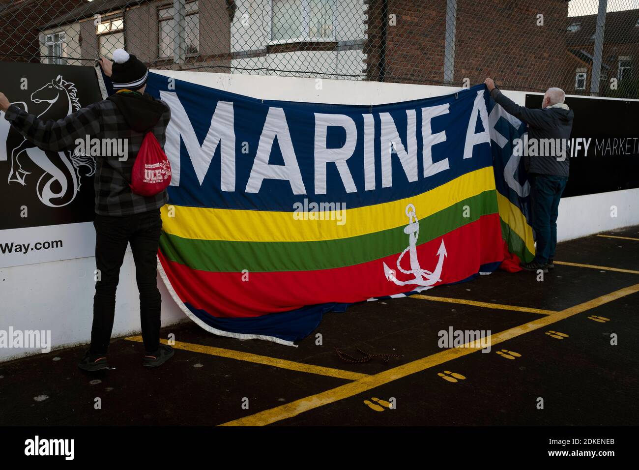 Deux supporters à la maison attachant un drapeau de club à une clôture avant Marine jouent Hyde United dans un FA Trophy première cravate à la Marine Travel Arena, anciennement connu sous le nom de Rossett Park, à Crosby. En raison de la réglementation du coronavirus qui avait suspendu les matchs de ligue, les seuls joueurs des Merseysiders ont participé aux compétitions de coupe, y compris leur prochaine égalité contre Tottenham Hotspur lors de la coupe FA troisième tour. Marine a gagné le match par 1-0, regardé par une capacité autorisée de 400, avec les visiteurs ayant deux hommes envoyés dans la seconde moitié. Banque D'Images