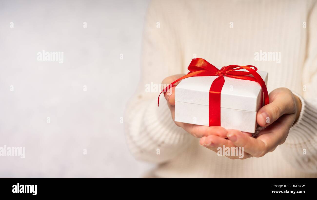 Femme de beauté mains tenant boîte cadeau avec noeud rouge sur fond blanc, gros plan. Couleurs pastel, espace de copie pour le texte. Cadeau de Saint-Valentin. Bannière pour Banque D'Images