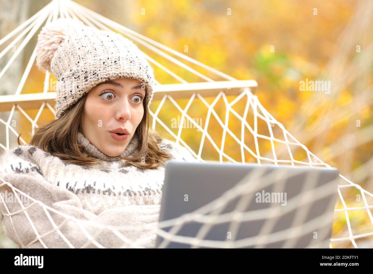 Un touriste stupéfait allongé sur un hamac qui vérifie les informations surprenantes sur un ordinateur portable en automne dans une forêt Banque D'Images
