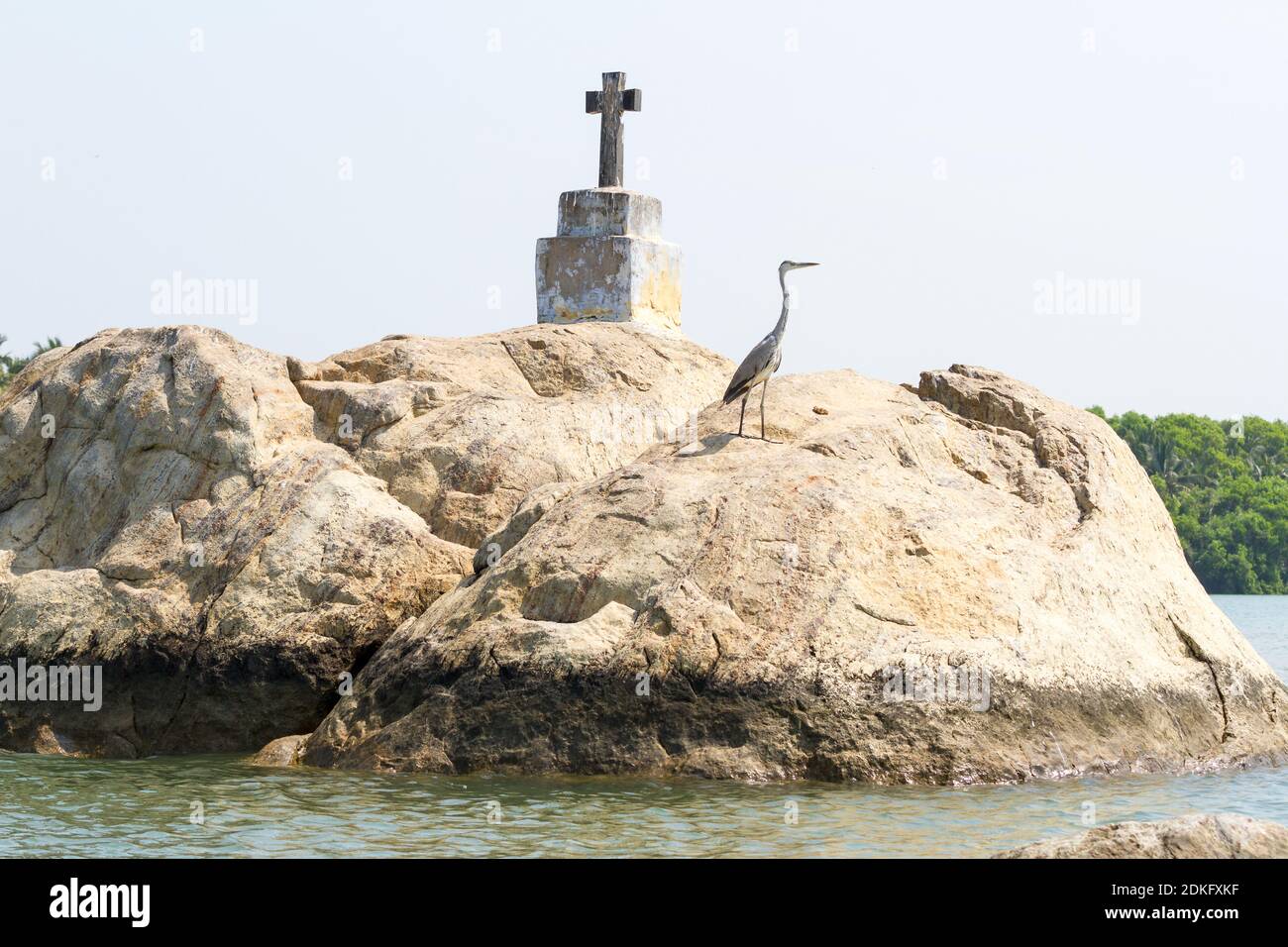 La croix chrétienne et l'oiseau de héron (aigrette) sur les petites îles rocheuses dans les eaux du Kerala, dans le sud de l'Inde. Banque D'Images