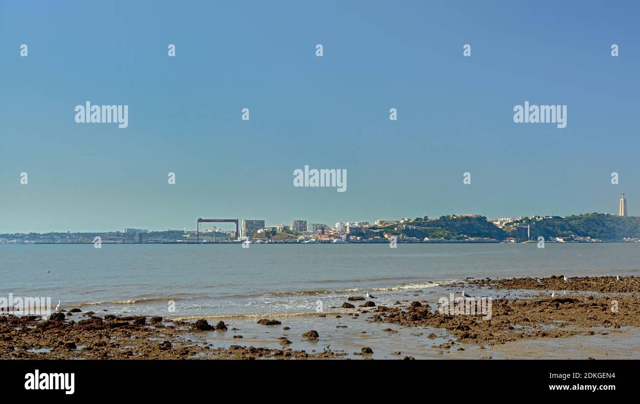 Marée basse sur le Tage, montrant les rochers du fond du fleuve, avec le port d'Almada et la statue de Christo Rei en arrière-plan Banque D'Images