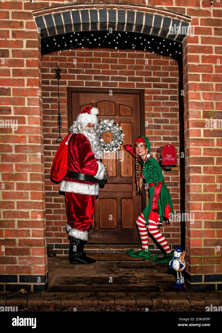 Royaume-Uni, Quorn - décembre 2020 : le Père Noël et un Elf se faufilent devant une porte lorsqu'ils livrent des cadeaux Banque D'Images