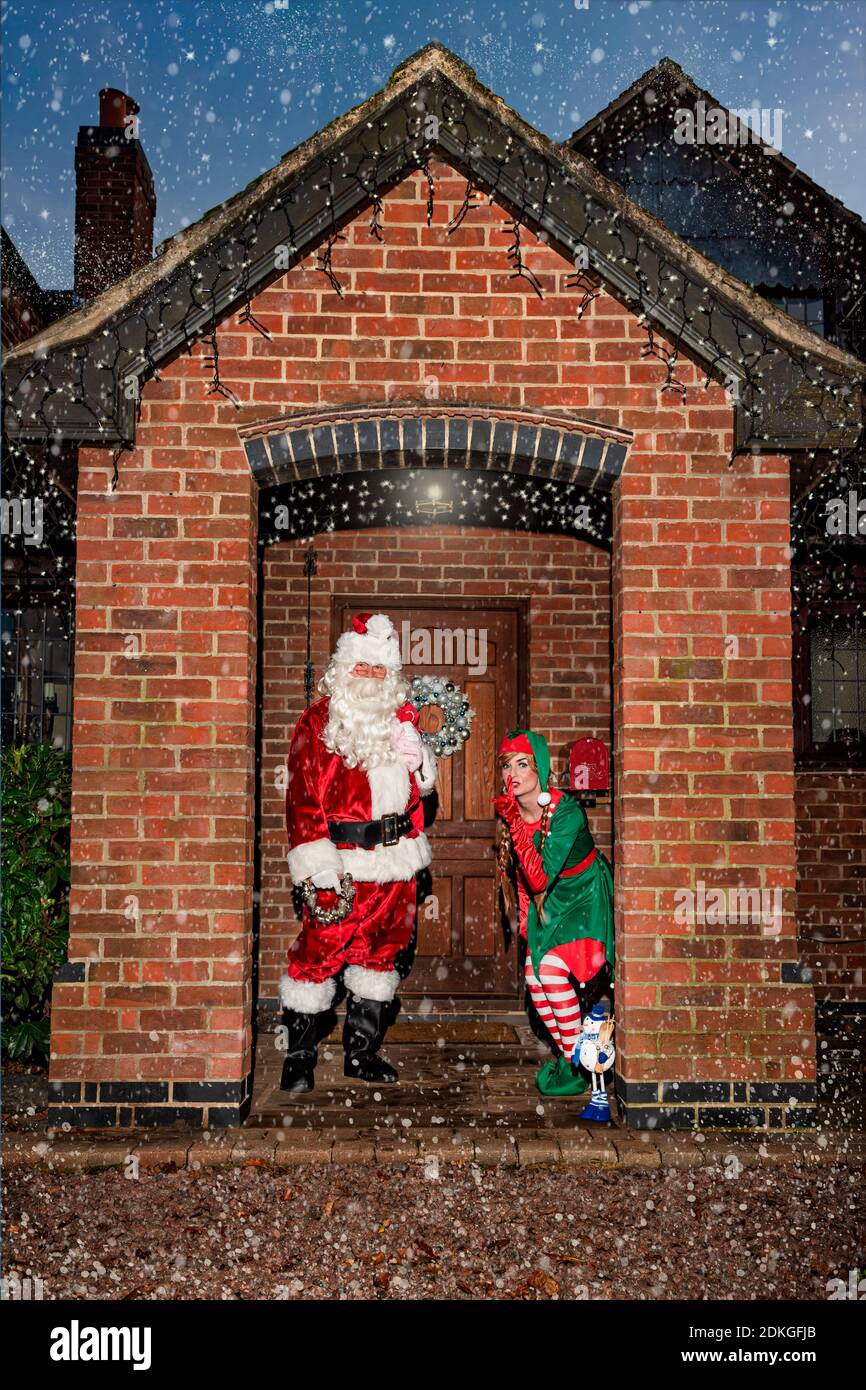 Royaume-Uni, Quorn - décembre 2020 : le Père Noël et un Elf se faufilent devant une porte, dans la neige, comme ils livrent des cadeaux Banque D'Images