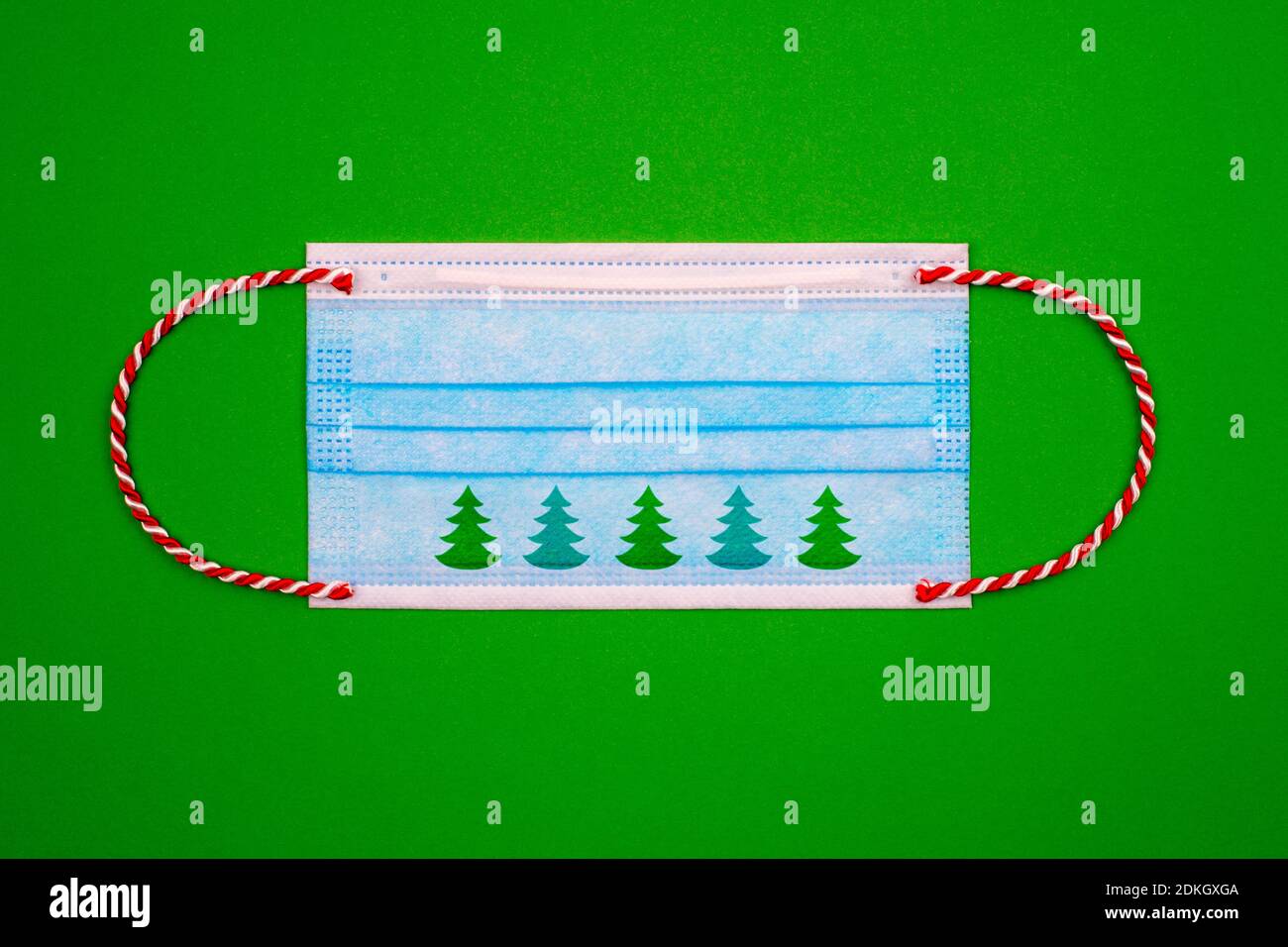 Masque médical bleu avec ruban de noël rouge et blanc au lieu de caoutchouc et arbre de noël vert sur fond de papier vert. Flat Lay.Covid pendant Banque D'Images