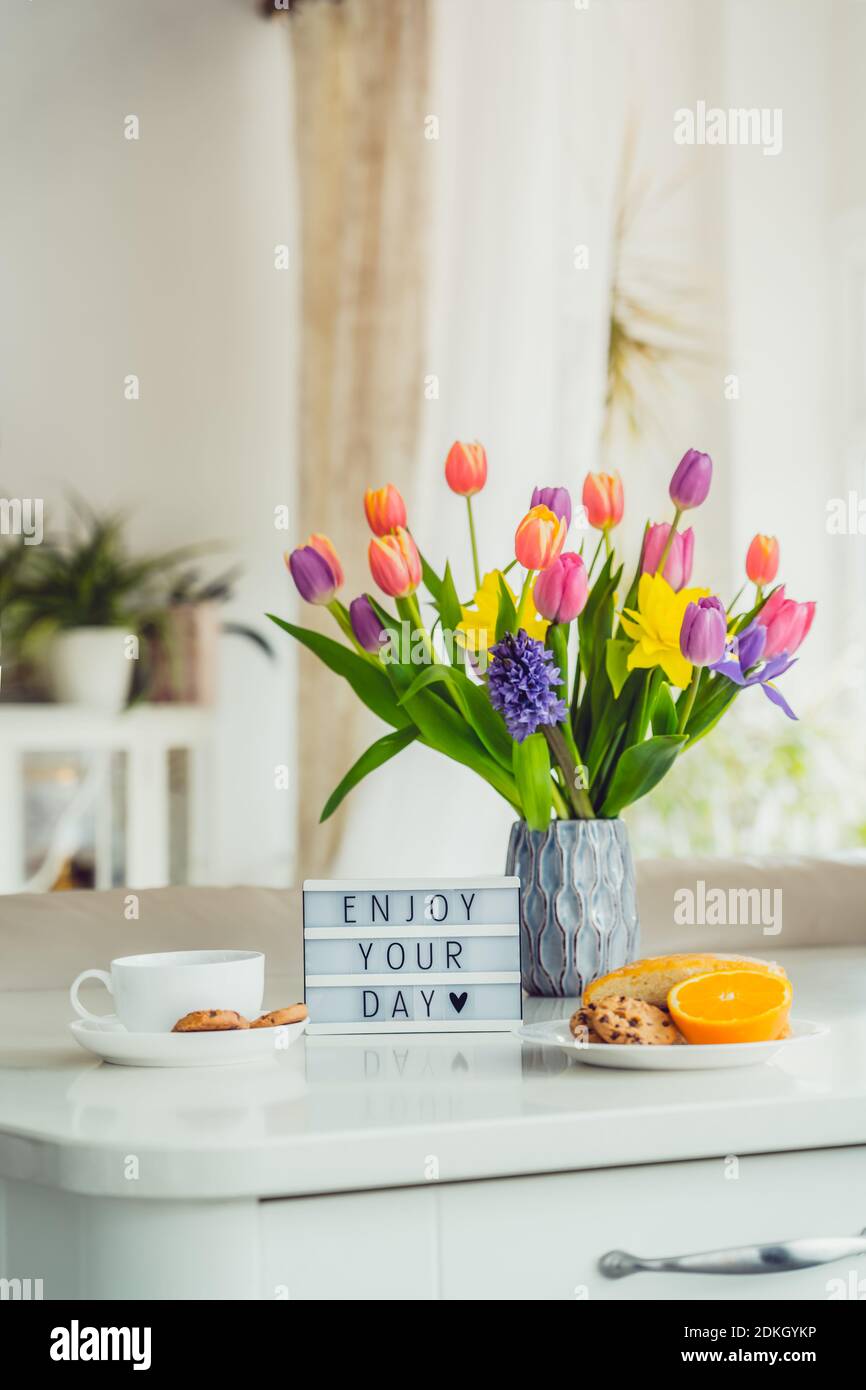 Concept Bonjour. Petit déjeuner romantique - fleurs fraîches, tasse de boisson chaude, petits gâteaux, orange, visionneuse avec message Profitez de votre journée sur une table en marbre avec Banque D'Images