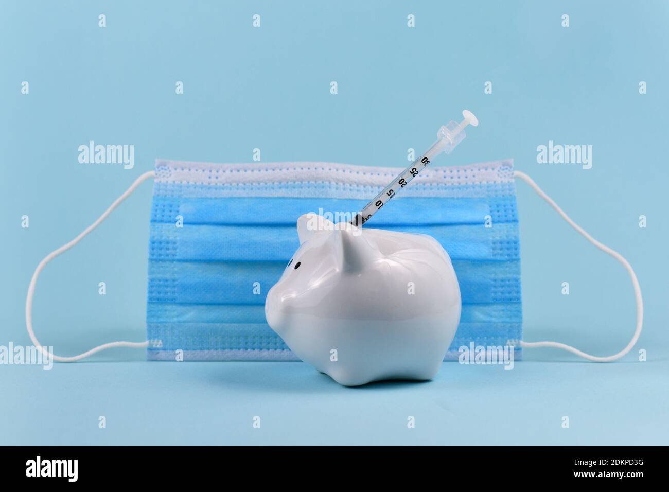 Dépenses de vaccin contre le virus Corona concept avec banque de porc blanche, seringue et masque médical sur fond bleu Banque D'Images