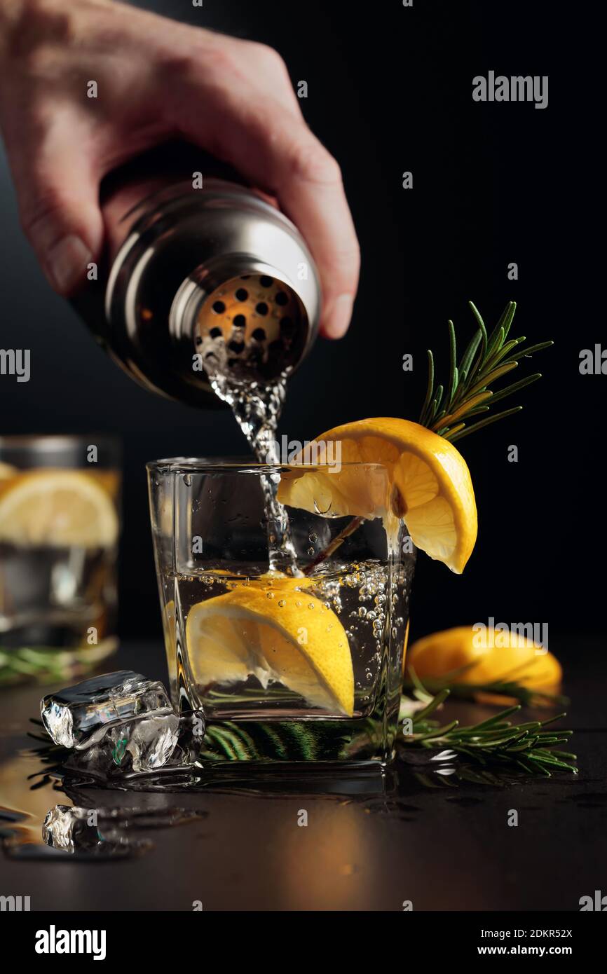 Cocktail Gin et tonique au citron et au romarin. Le barman verse un  cocktail d'un shaker dans un verre Photo Stock - Alamy