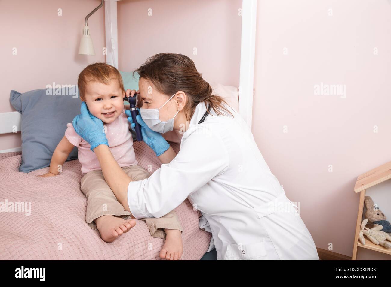 Le pédiatre examine l'oreille de la petite fille à la maison pendant la quarantaine pandémique COVID-19 du coronavirus. Médecin utilisant l'otoscope (auriscope) pour vérifier le canal auditif a Banque D'Images