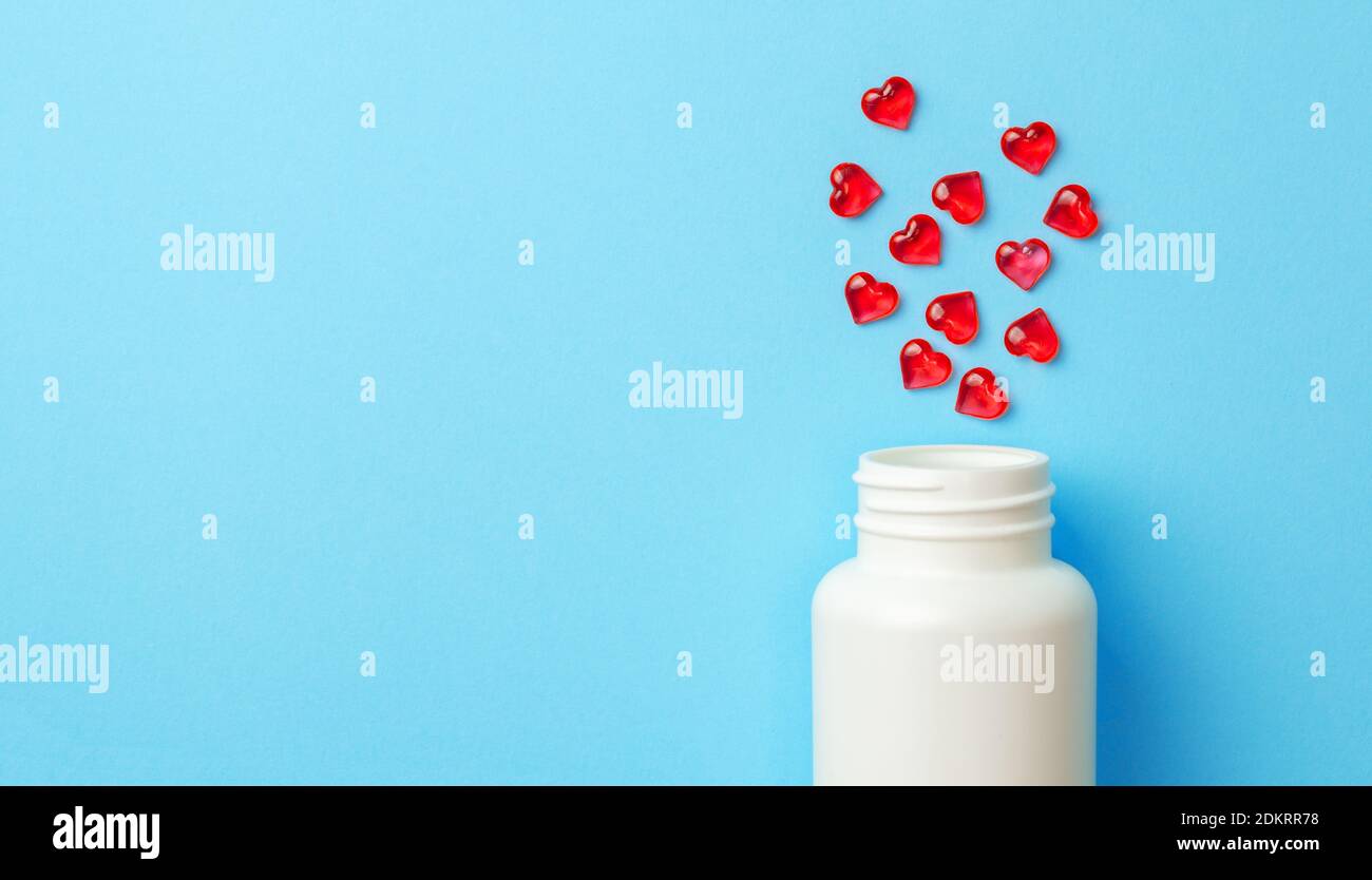 Pilules rouges en forme de coeur avec bouteille sur fond bleu. Copier l'espace pour le texte. Banque D'Images