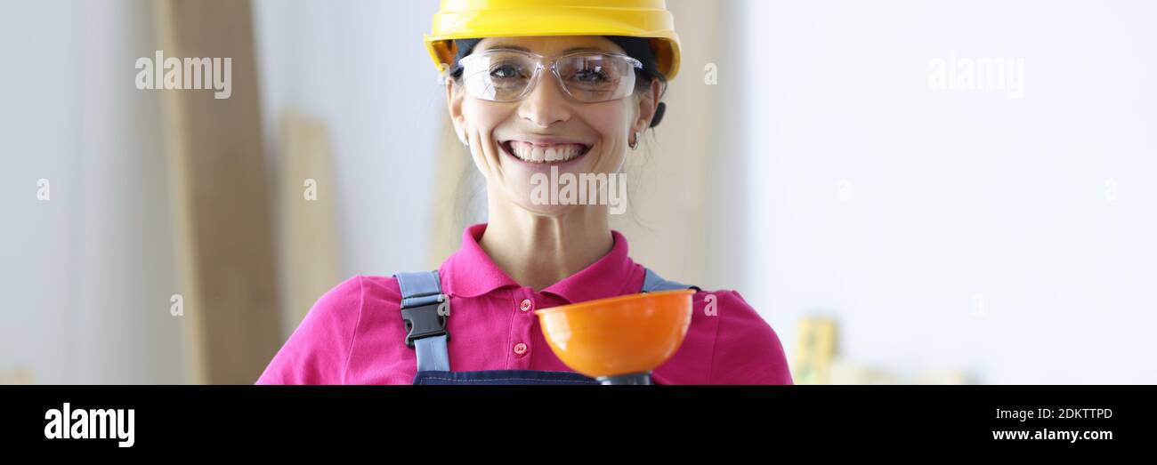 Femme souriante dans un casque de sécurité jaune et des lunettes tenant le piston en main Banque D'Images