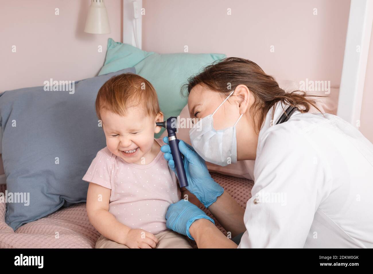 Le pédiatre examine l'oreille de la petite fille à la maison pendant la quarantaine pandémique COVID-19 du coronavirus. Médecin utilisant l'otoscope (auriscope) pour vérifier le canal auditif a Banque D'Images