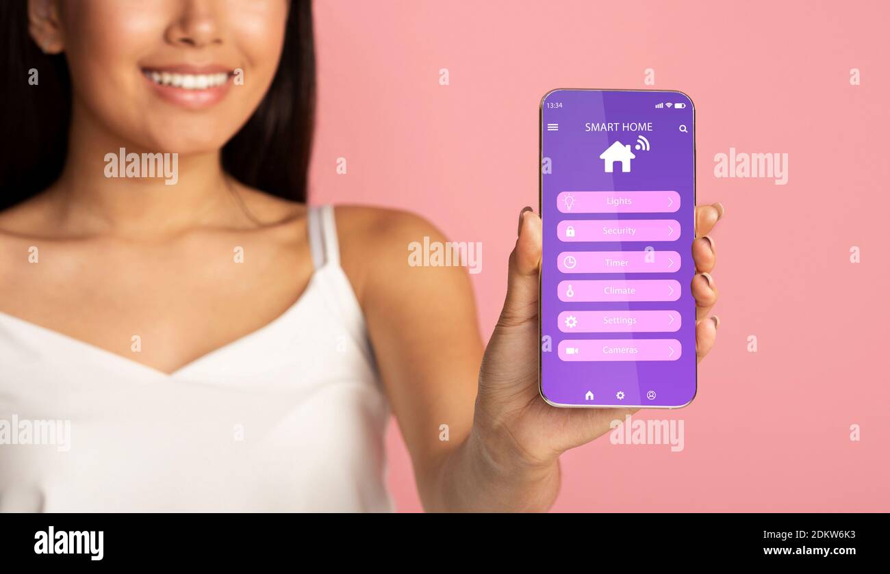 Jeune femme méconnaissable annonçant l'application mobile smarthome sur le téléphone sur fond rose, collage Banque D'Images