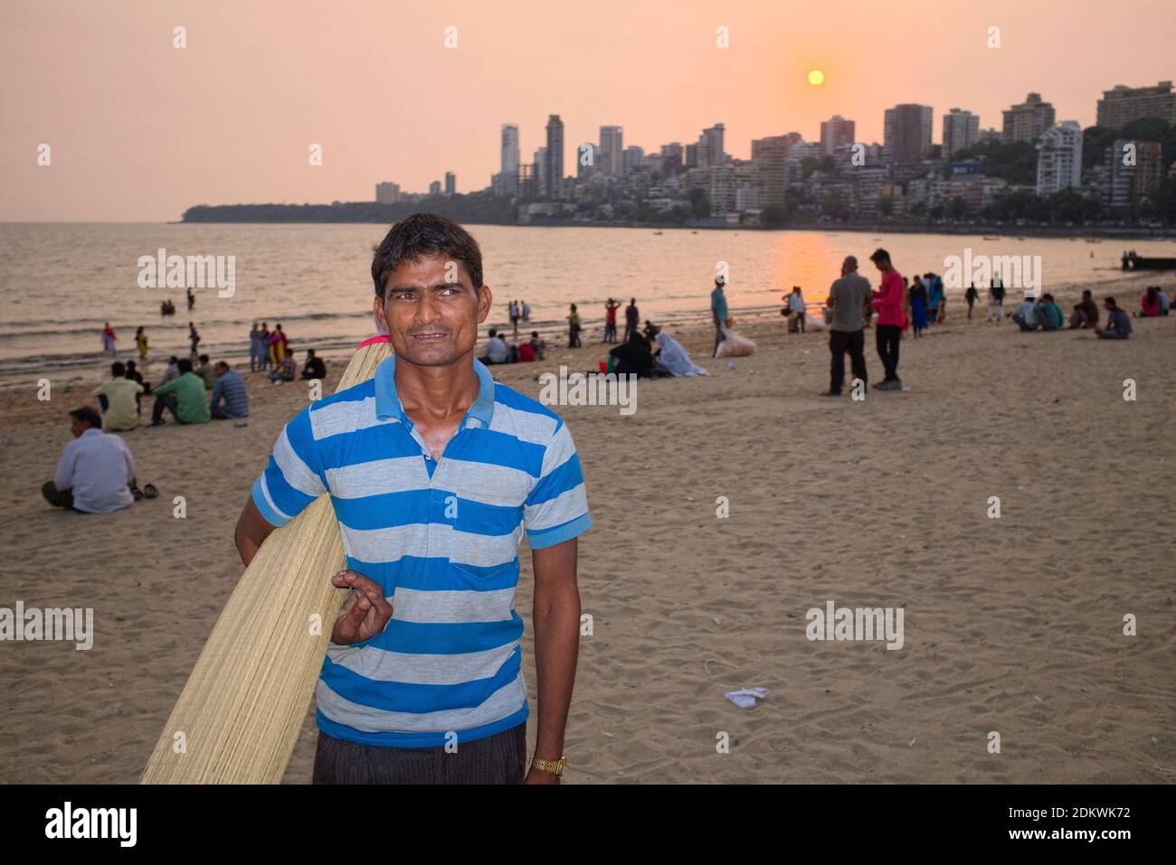 Un homme louant des tapis aux visiteurs à Chowpatty Beach, Girgaum, Mumbai, Inde, avec un coucher de soleil derrière les immeubles d'appartements de la zone posth Walkeshwar Banque D'Images