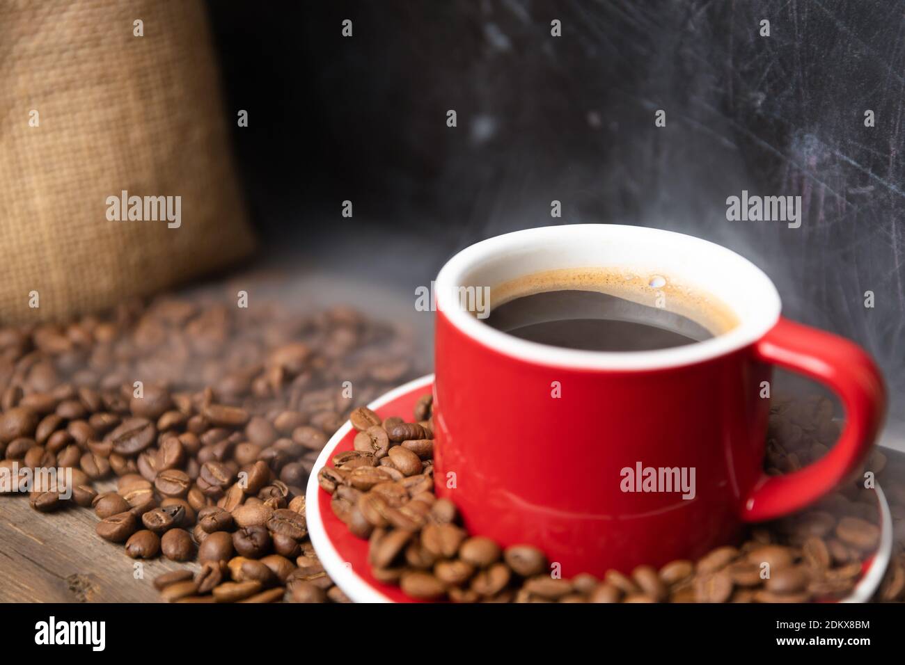 Tasse de café rouge avec grains de café sur fond texturé foncé. Concept d'énergie fraîche du matin. Banque D'Images
