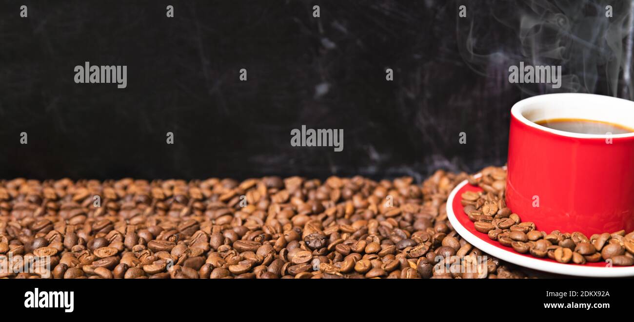 Tasse de café rouge avec grains de café sur fond texturé foncé bannière avec espace de copie. Concept d'énergie fraîche du matin. Banque D'Images