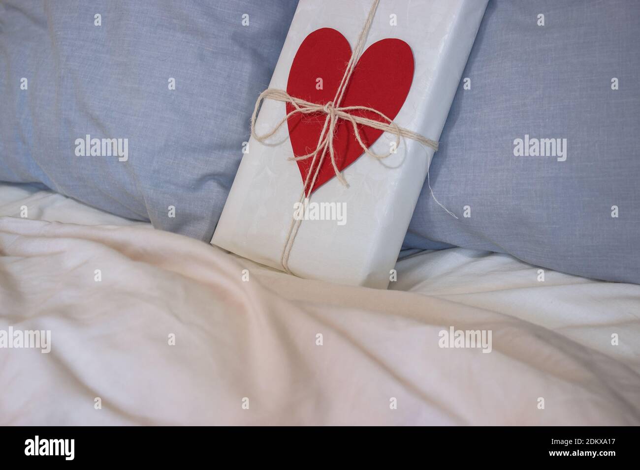 Un cadeau avec un ruban et un coeur est placé sur le lit d'un couple aimant de la maison pour la Saint-Valentin. Cadeau de Saint-Valentin. 14 février 2021. Banque D'Images