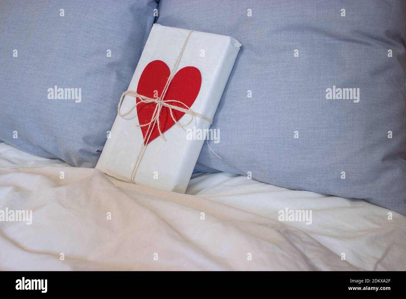 Un cadeau avec un ruban et un coeur est placé sur le lit d'une maison de couple aimant pour la Saint-Valentin 2021. Concept de la Saint-Valentin. Banque D'Images