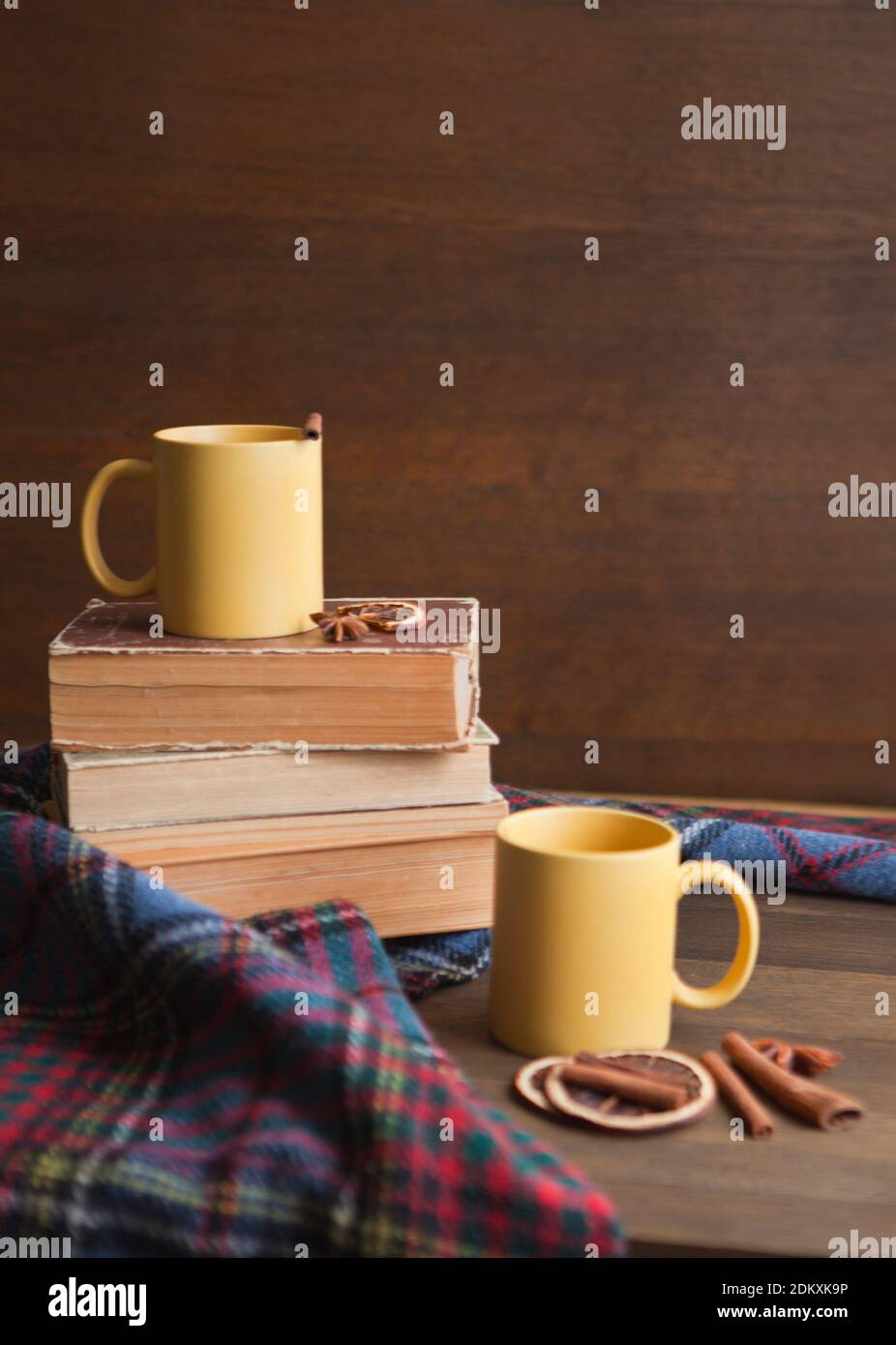deux tasses à thé jaunes avec fond de livres, une tasse en céramique avec cannelle, des livres et une couverture avec des rouleaux et de la cannelle Banque D'Images