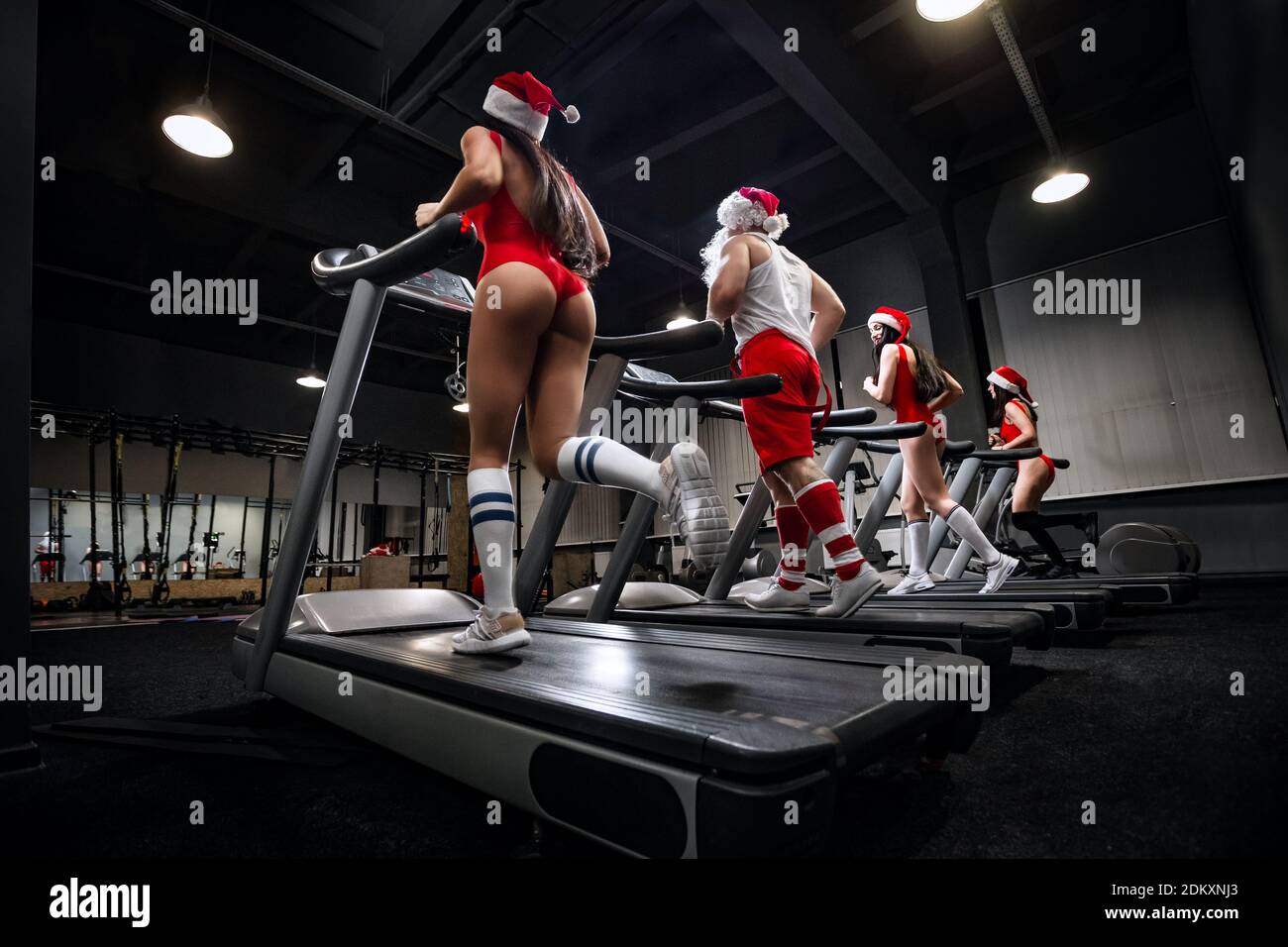 Bodybuilder Santa et sexy filles en rouge maillot de bain sont en cours d'exécution dans une salle de gym. Entraînement de la veille de Noël. Banque D'Images
