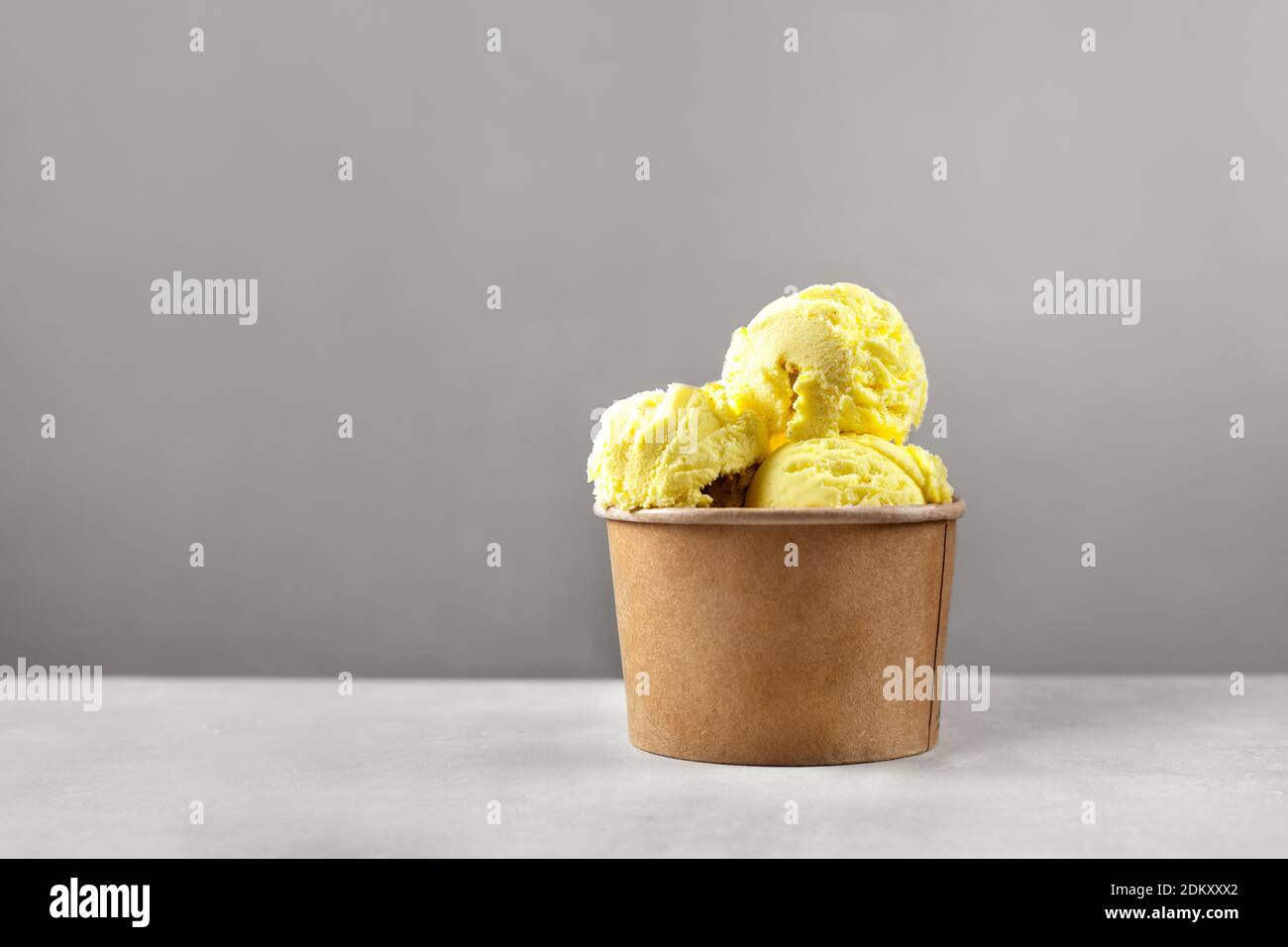 La crème glacée jaune se ramasse dans un gobelet en papier sur fond gris Banque D'Images