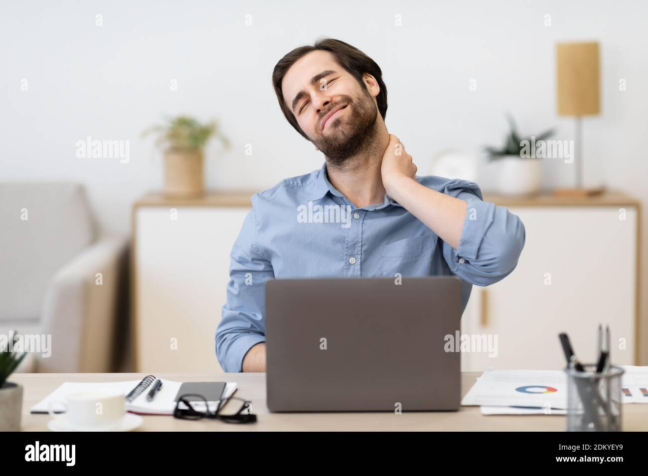 Homme d'affaires fatigué massant cou assis à l'ordinateur portable au bureau Banque D'Images
