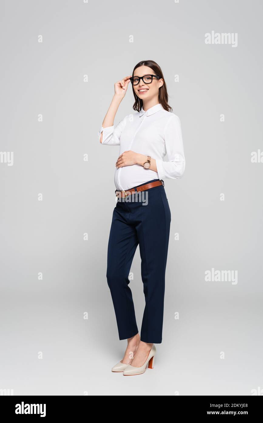 jeune femme d'affaires souriante enceinte dans des lunettes isolées sur le gris Banque D'Images