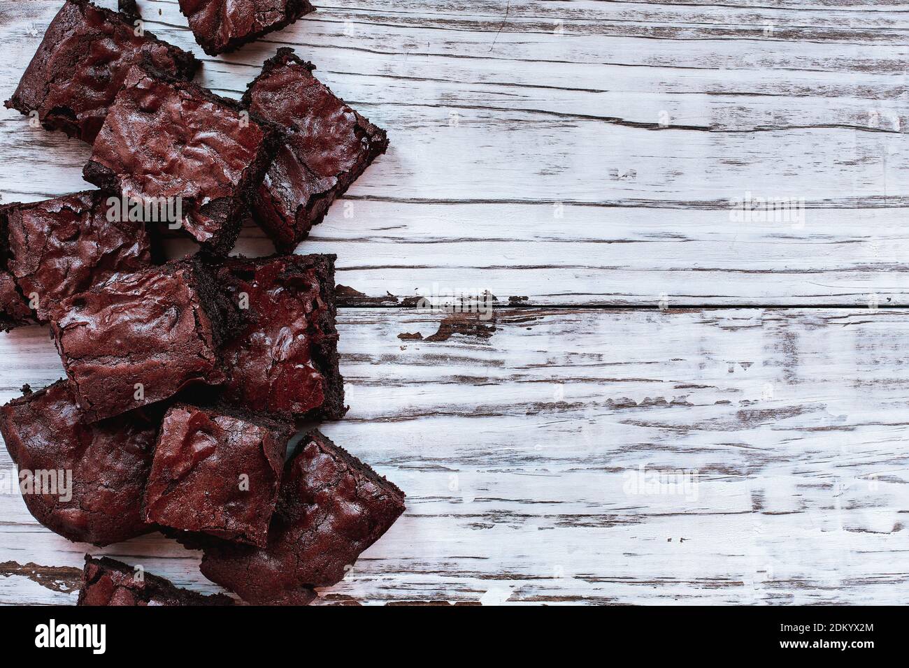 Squares of delicious, homemade fudgy brownies stacked a white rustic wooden table background. Image shot from top view overhead. Banque D'Images