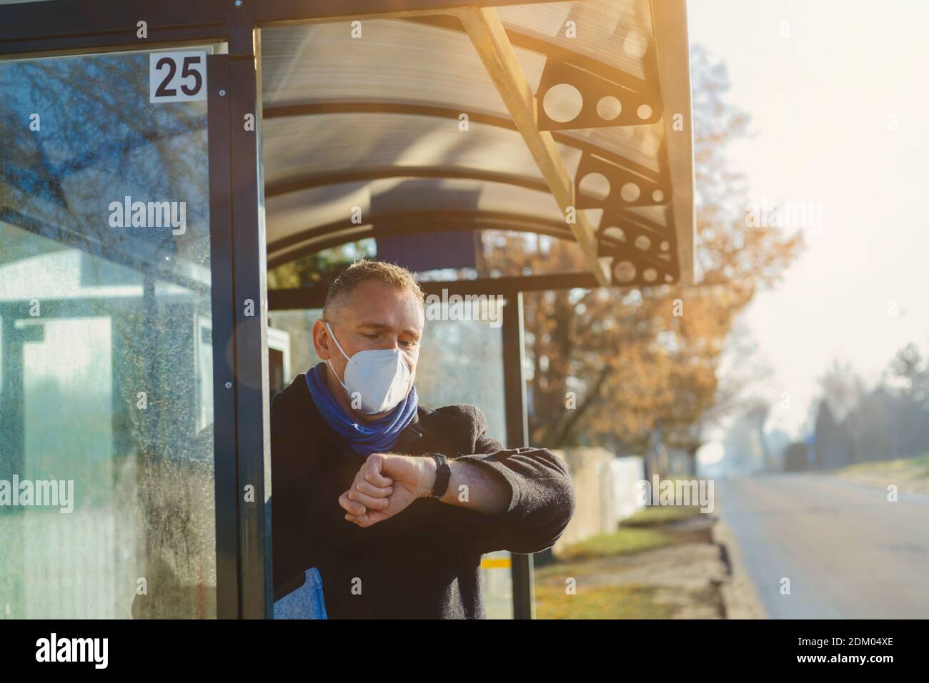 Man se tient à l'arrêt de bus qui attend le bus dans un masque antiviral Banque D'Images