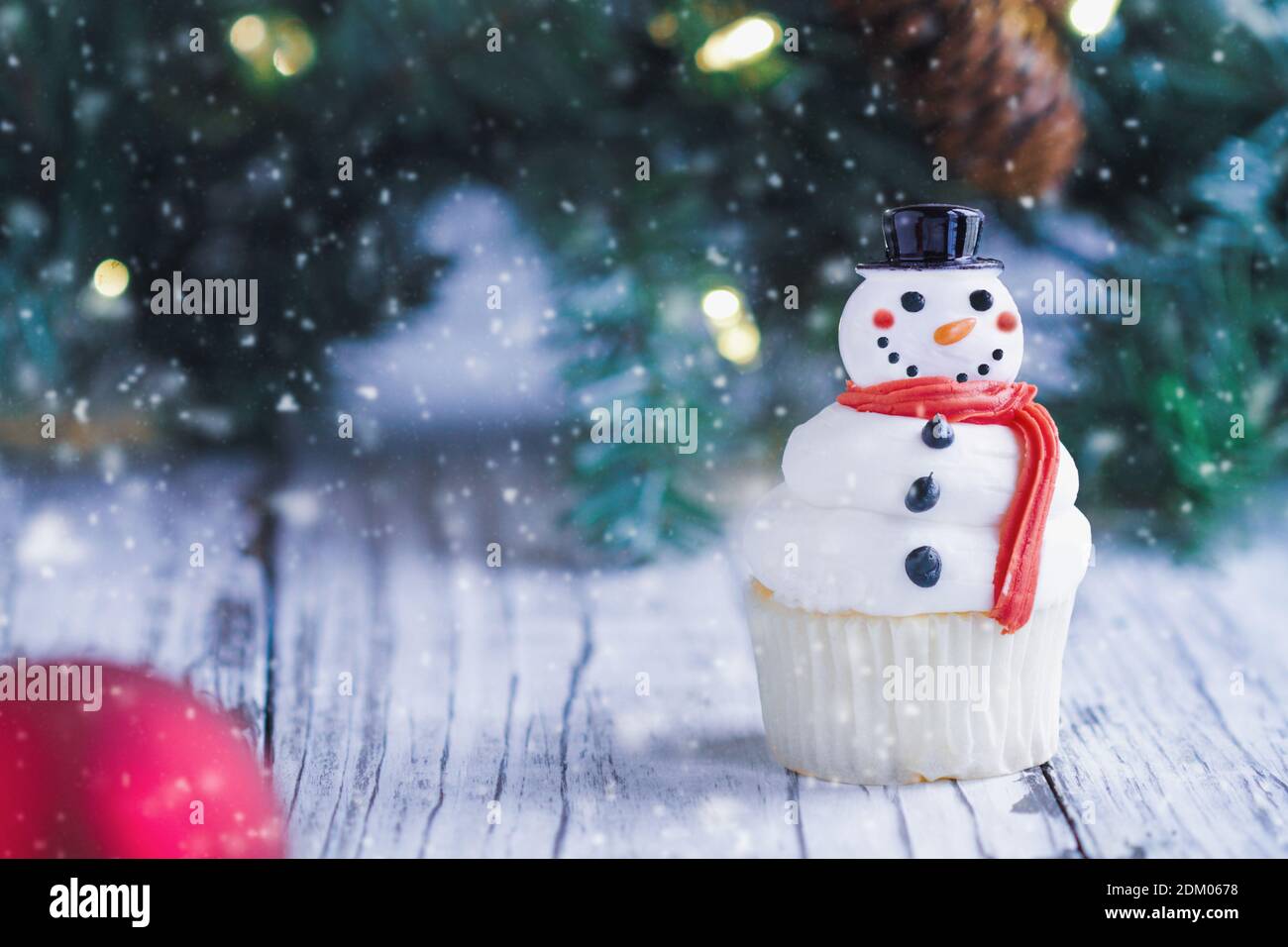 Gâteau de Noël glacé et joyeux bonhomme de neige avec nez de carotte, chapeau de père noël et foulard. Mise au point sélective avec un premier plan et un arrière-plan flous. Banque D'Images