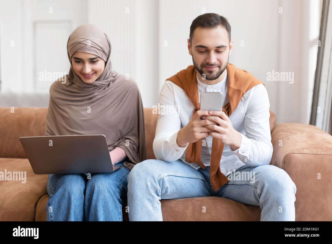 Couple musulman utilisant un ordinateur portable et un smartphone assis sur un canapé intérieur Banque D'Images