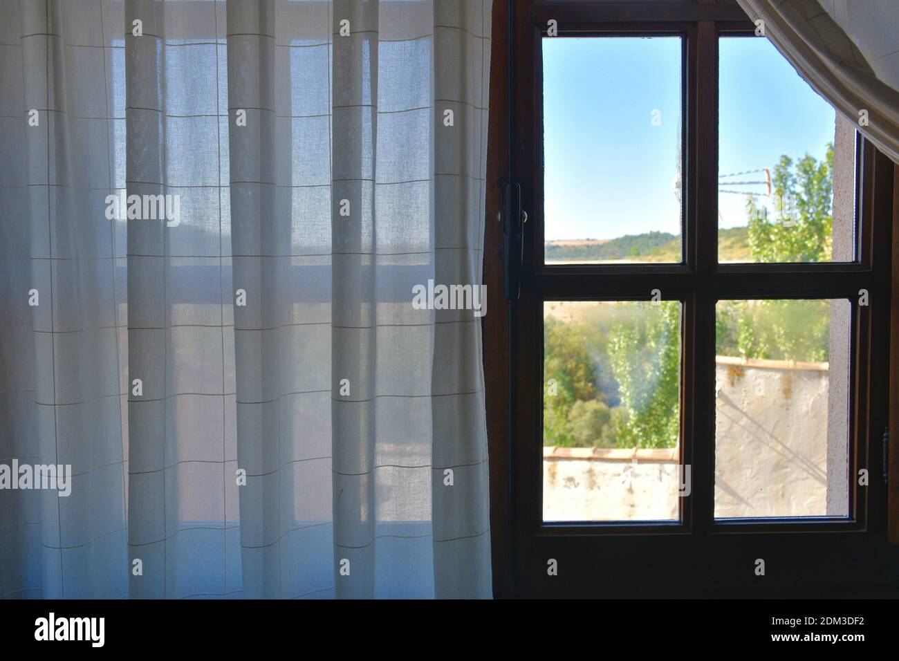 Fenêtre en bois avec rideau blanc et vue sur les maisons, les arbres et le ciel. Banque D'Images