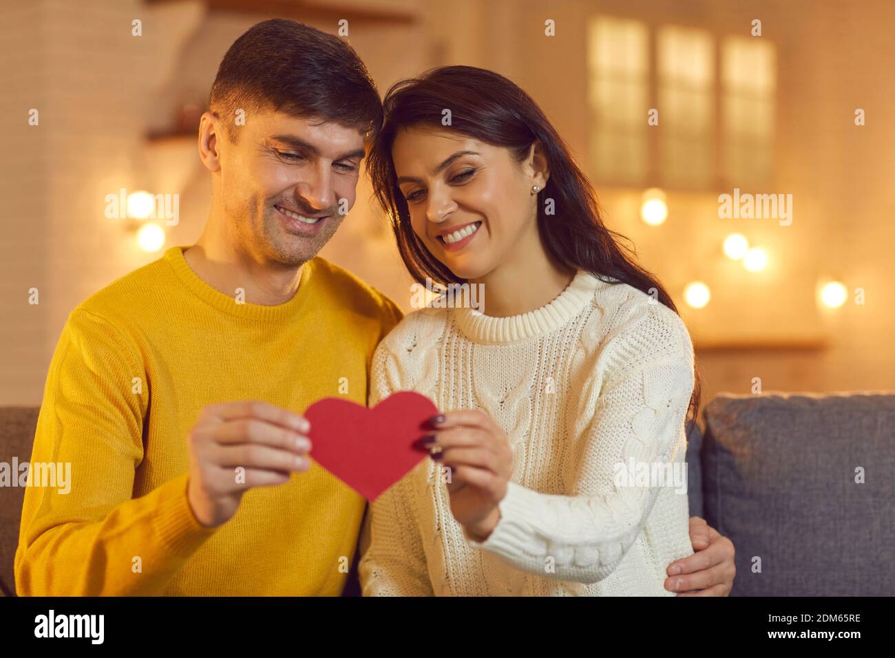 Jeune amoureux heureux couple assis sur un canapé et tenant rouge coeur décoratif ensemble Banque D'Images