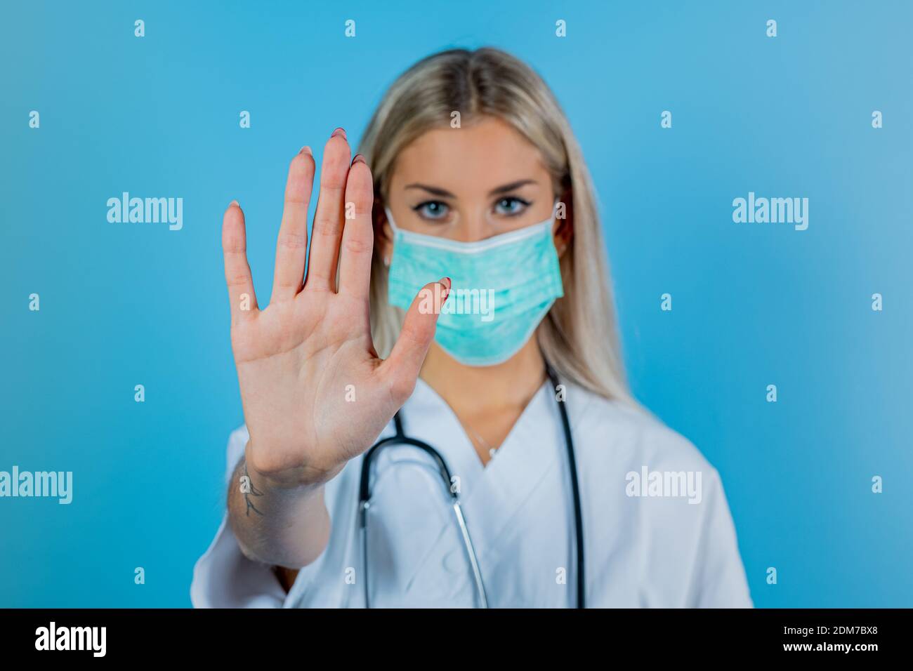 Une jeune belle femme médecin en manteau blanc, en masque bleu. L'infirmière montre à la main s'arrêter à la main sur la période du coronavirus. Médecin dans le masque de protection symb Banque D'Images