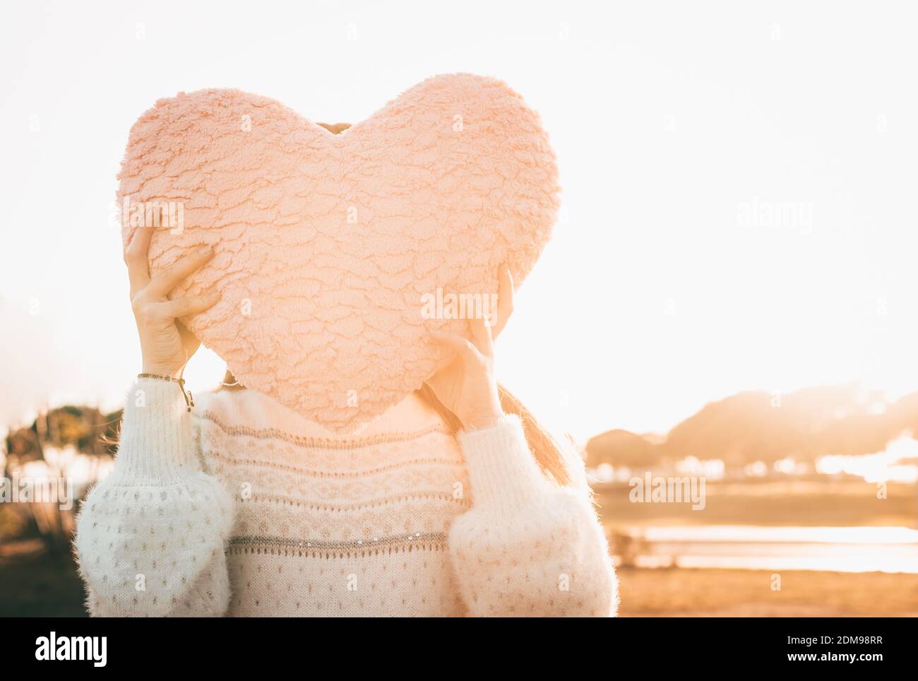 Fille tenant UN coussin en forme de coeur rose couvrant son visage Banque D'Images