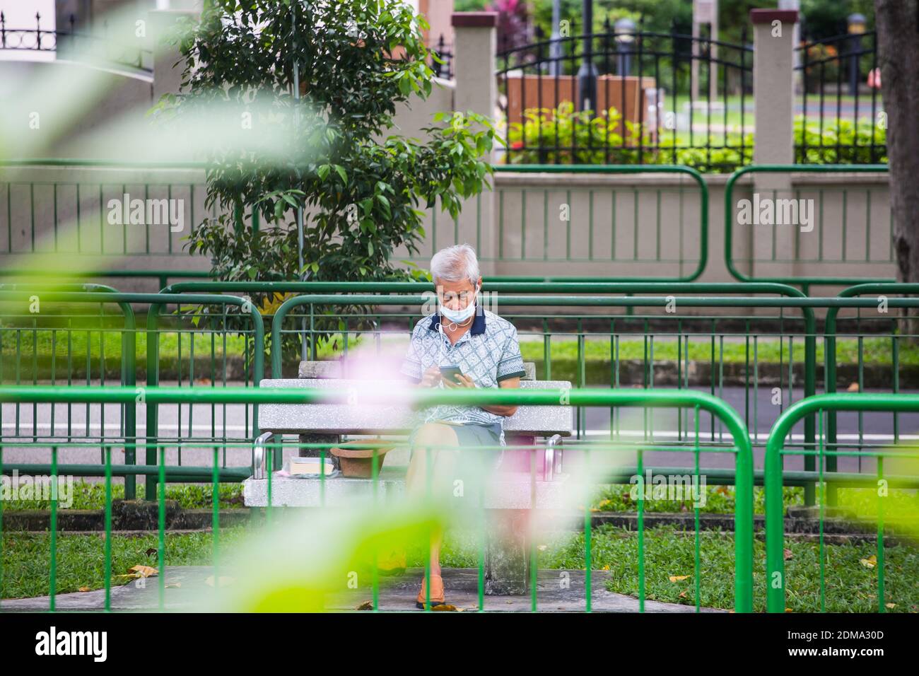 Comme la pandémie est toujours en cours, les Singapouriens sont très disciplinés pour porter un masque, voici un vieil homme qui porte un masque assis dans le parc public. Banque D'Images