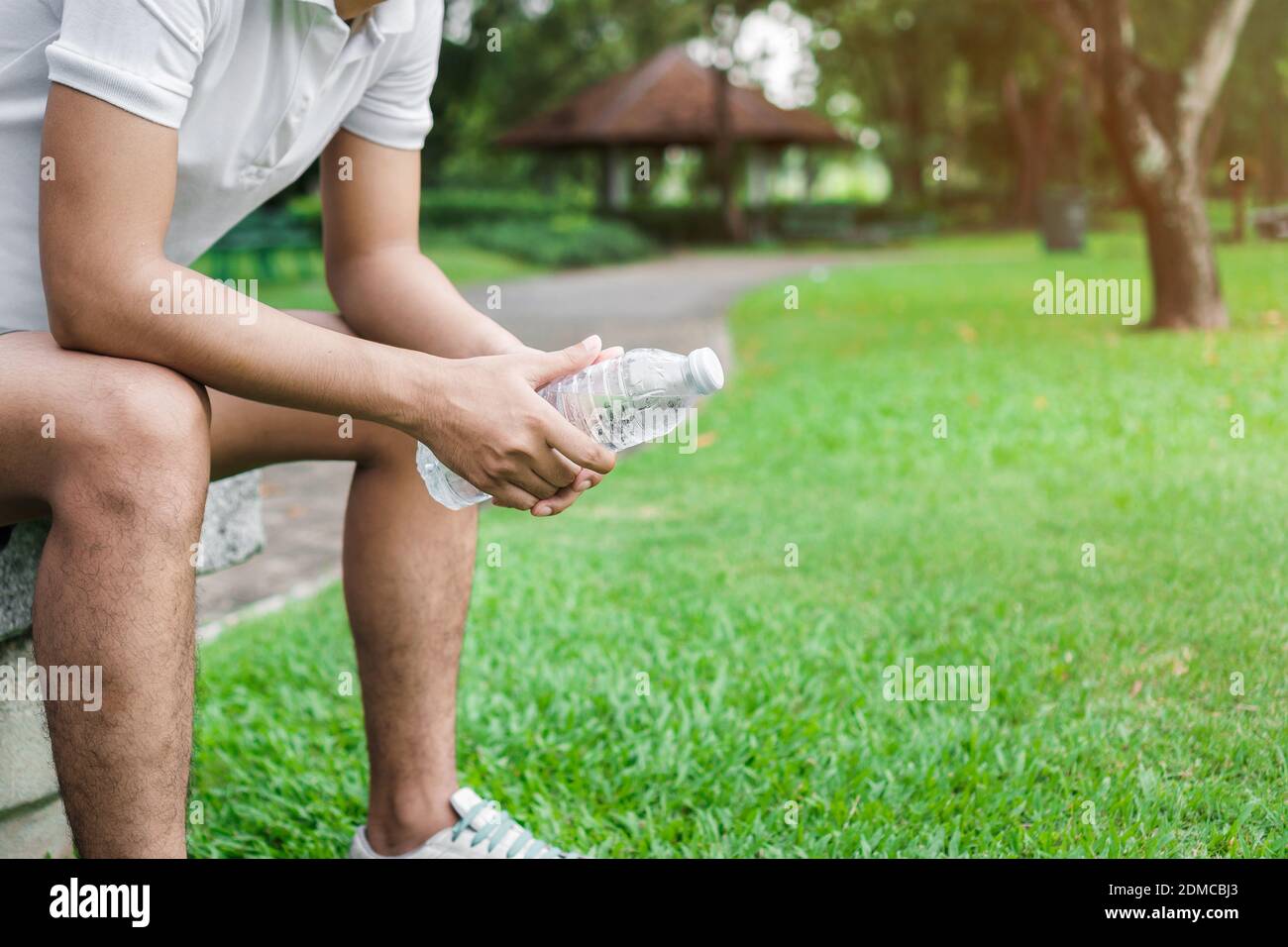 Exercice et concept sain, jeune asiatique homme coureur relaxant tenant une  bouteille d'eau potable et assis sur le banc dans le parc à l'extérieur  après le sport tôt le matin Photo Stock -