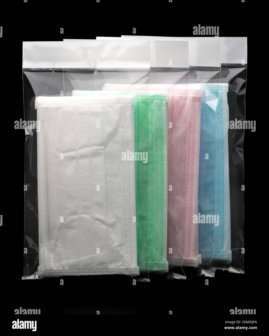 Contour d'oreille vert, rose, bleu clair et blanc masque jetable dans un  sac en plastique se chevauchant, utilisé pour couvrir la bouche et le nez.  Il protège contre les liquides organiques et