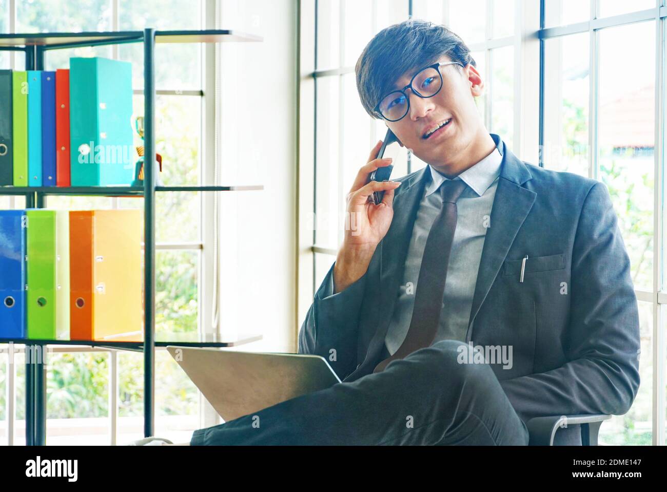 Homme d'affaires asiatique assis et de parler avec le client par smartphone près fenêtre dans la salle de réunion Banque D'Images