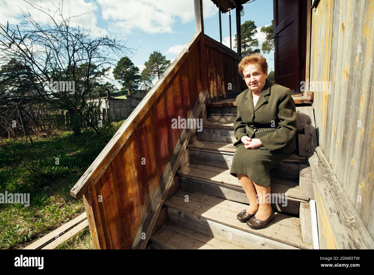 Vieille femme assise sur le porche d'une maison de village. Banque D'Images