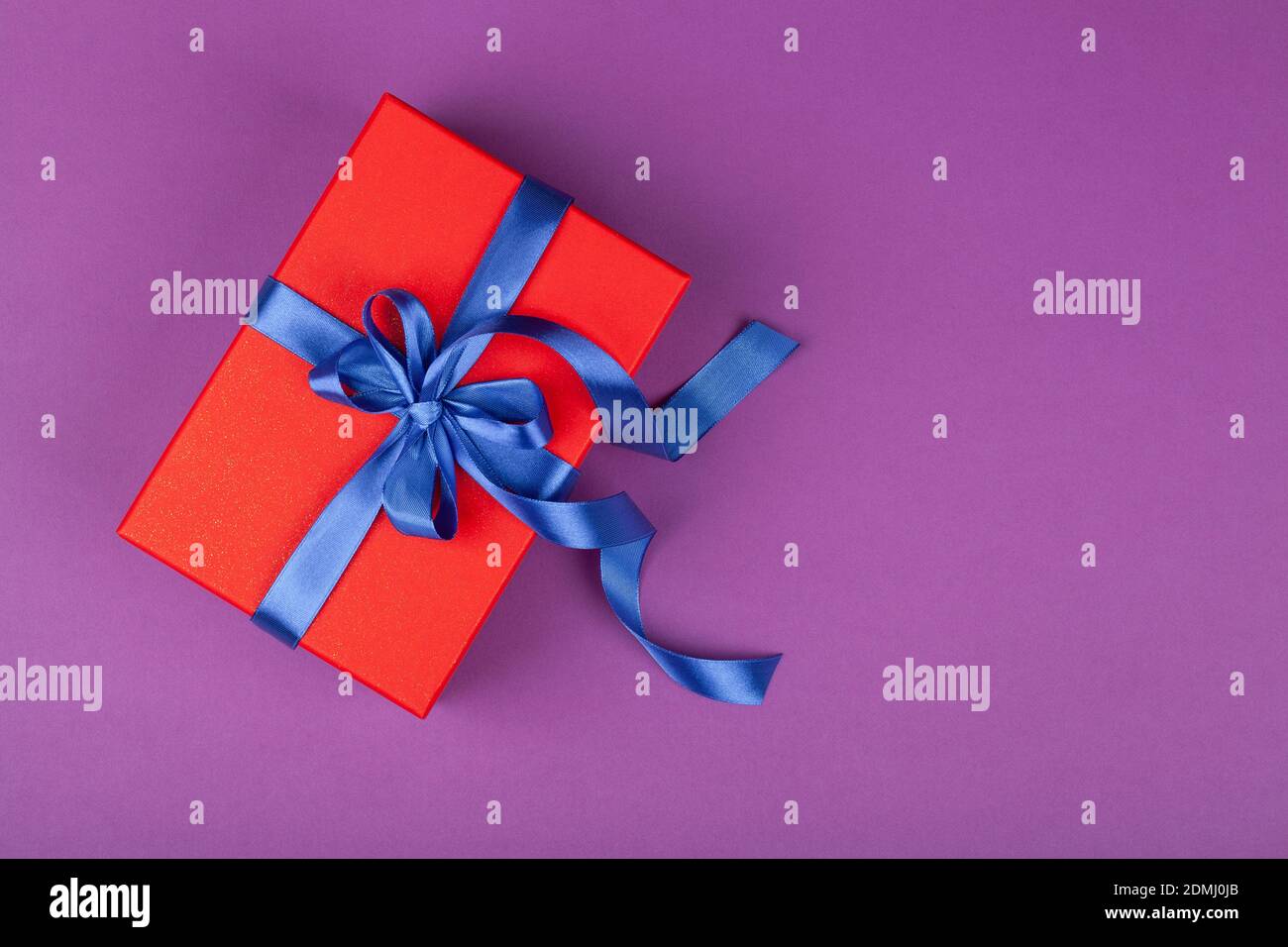 boîte cadeau ou cadeau rouge avec ruban bleu sur fond violet. composition pour anniversaire, saint-valentin, fête des mères ou mariage. vue du dessus espace pour les copies Banque D'Images boîte cadeau ou cadeau rouge avec ruban bleu sur fond violet. composition pour anniversaire, saint-valentin, fête des mères ou mariage. vue du dessus espace pour les copies Banque D'Images