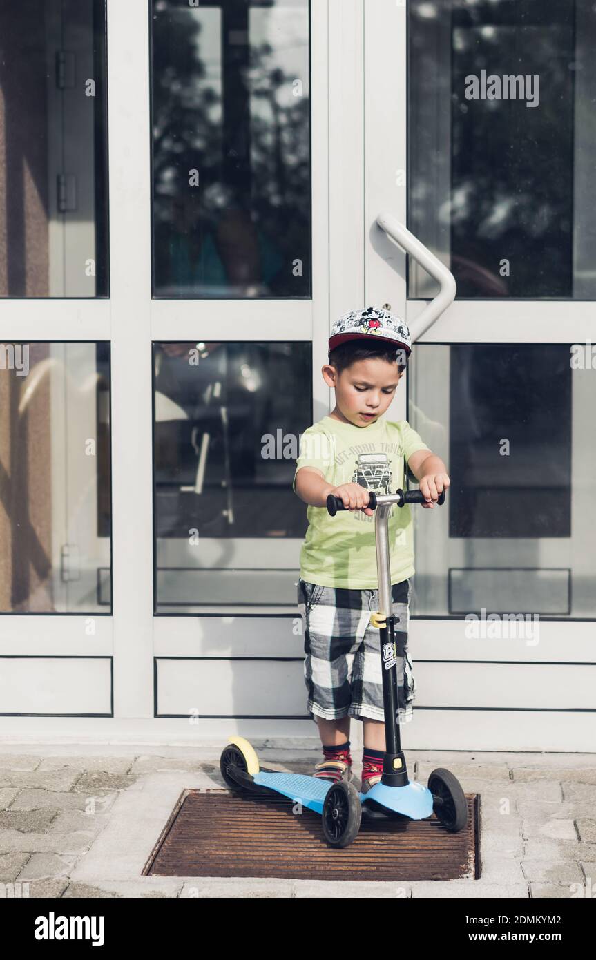 POZNAN, POLOGNE - 18 août 2017 : jeune garçon debout sur un petit scooter d'enfant devant une porte fermée Banque D'Images